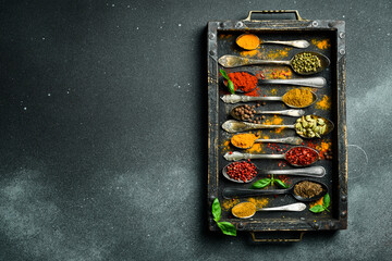 A set of colored spices in a wooden box. On a black slate background. Top view.