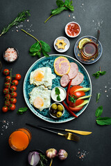 English breakfast. Fried eggs, salami, bacon and vegetables. Tea and sweets. On a dark slate background.