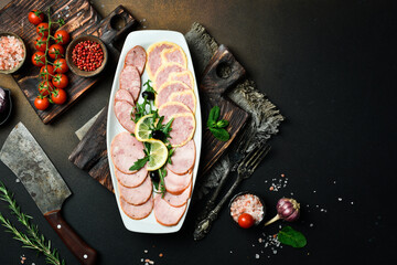 Cutting different types of salami on a plate. On a dark slate background.