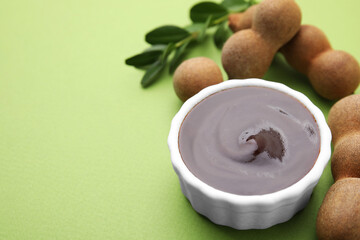 Bowl of tasty tamarind sauce and fresh pods on light green table. Space for text