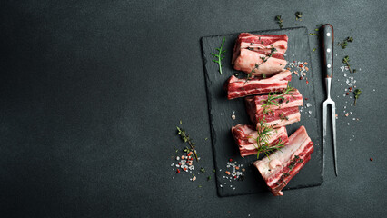 Raw sliced veal short spare loin ribs on a marble board. Black background. Top view. Copy space