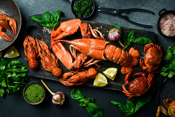 crustacean seafood: lobster, crab and crayfish with lemon and basil on a black slate board. Top view.