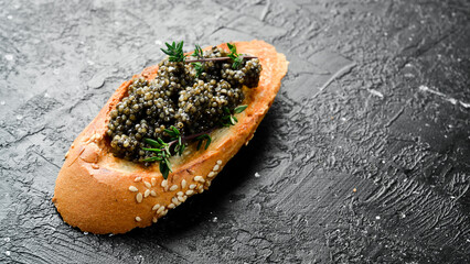 Sandwiches with black caviar, caviar in a bowl. On a black stone background. Rustic style.