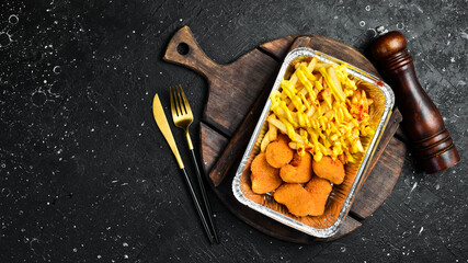 Fast food. French fries and chicken nuggets in a disposable dish. On a wooden board.