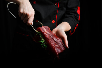 The chef is holding a piece of raw veal. Meat. On a black background.