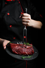 The chef is holding a plate with a piece of raw veal. Meat. On a black background.