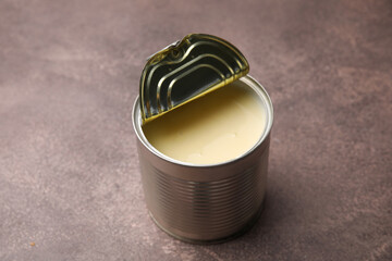 Open tin can with condensed milk on brown table