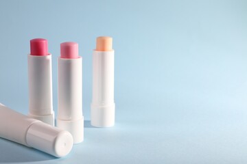 Different lip balms on light blue background, space for text
