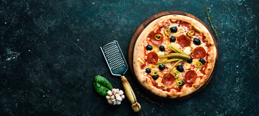 Delicious homemade pizza with pepperoni and vegetables. Home delivery of food. On a black stone...