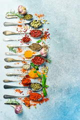 Spices and herbs in spoons on a gray stone background. Top view. Free space for text.