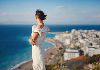Beautiful Asian young woman in white dress outdoor in flower field under Rhodes city and above sea...