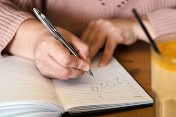 Woman's hand writing 2024. New Year Routine, resolutions on desk. Cafe, restaurant interior...
