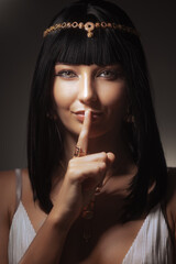 Obraz premium Historical mystery and beauty secrets. Queen Cleopatra fashion beauty female portrait in studio with finger on her lips. Amazing seductive young woman with perfect Egyptian make-up and ancient pharaoh