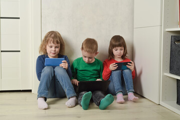 Children sit on the floor and use electronics to learn, play and communicate. Generation alpha,...