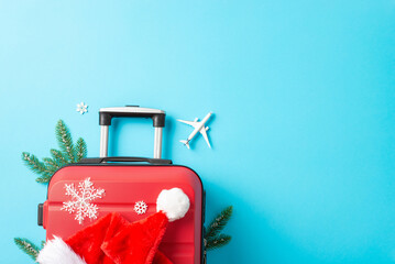 Santa Claus is en route to your party! Overhead shot of a red suitcase, tiny airplane, Santa's hat,...