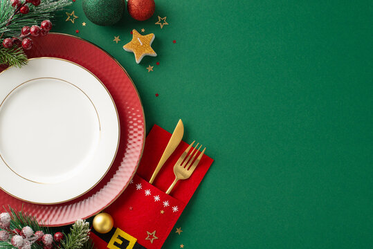 Jolly holiday table setting. Top-view image of dishes, charming cutlery pocket, star candle, confetti, ornaments, frosty fir twigs, mistletoe berries on green backdrop, open space for text