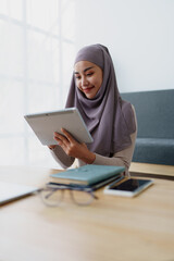 Female Muslim employee uses tablet to work at office.