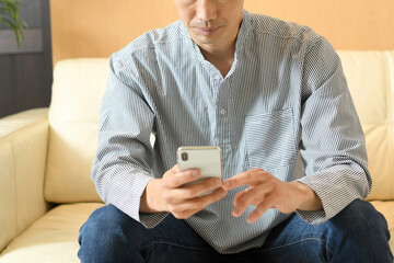 真面目な表情でスマートフォンを見る私服姿のアジア人の男性