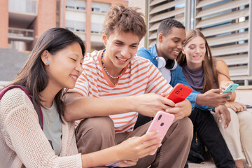 smiling multiracial students sitting outdoors using cell phone to chat online. University life concept