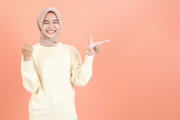 Happy beautiful Asian woman in cream sweater pointing fingers asides at copy space isolated over...
