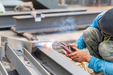 Worker welding steel beam for structure in building site.