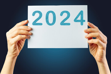 2024, Woman holding cardboard with number 2024 on blue background. Happy New Year