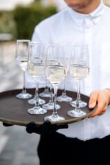 Waiter holding tray with glasses of white wine on terrace background