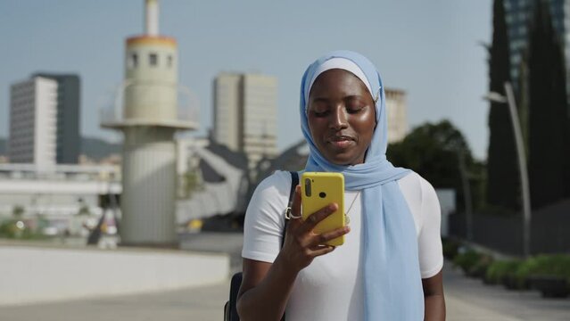 Modern African muslim woman using cell phone in the city