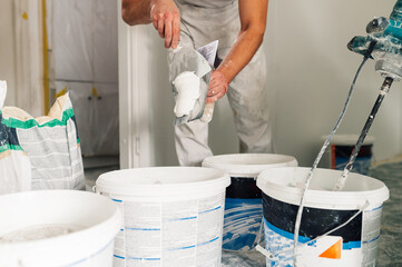 A worker holding tool and preparing material for plasterwork in house.