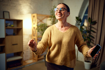 Adorable, cheerful woman listening music in headphones and relaxing while dancing in living room at home.