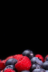 Colorful berries close-up on a black background, front view, macro photography. Blueberries, raspberries, strawberries. Concept of healthy nutrition. Vertical photo