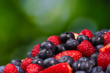 Close-up of juicy blueberries, strawberries, raspberries on a green blurred background. Colorful background of berries, summer food.