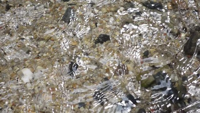 Neutral caucasian hand stamps and splashes into a clear stream of transparent water flowing along a beautiful stone and gravel riverbed. slow motion shot with smother water flow motion action