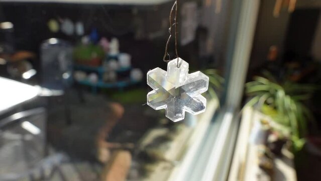 Six-core glass snowflake. Crystal element and transparent pendant jewelry reflects and refracts direct sunlight in an interesting way. Spectral decomposition of sunlight. prism colors in slow motion.