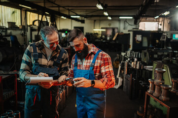 Fototapeta na wymiar Two engineers measuring and noting data about a metal piece in a factory.