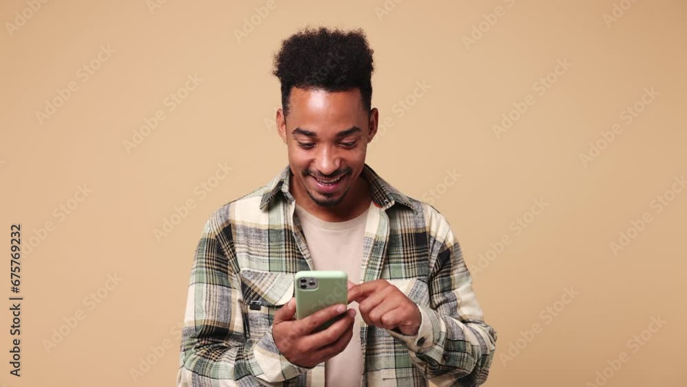 Wall mural Young dreamful pensive minded fun man of African American ethnicity he wear shirt casual clothes hold use mobile cell phone typing browsing chatting send sms isolated on plain beige brown background