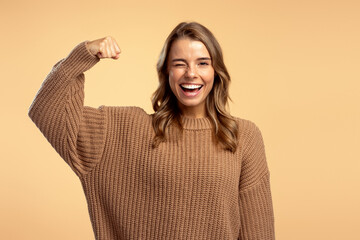 Strong excited woman wearing stylish brown sweater showing muscles looking at camera