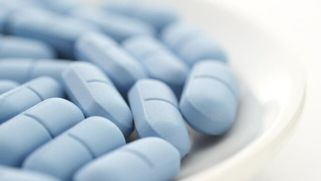 Heap of Blue pills in white plate close up, rotation. Pharmaceutical production