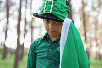 Portrait of a cute leprechaun boy in green clothes and high cylinder hat decorated with shamrocks