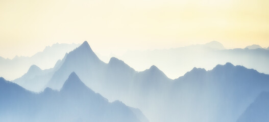 Mountain range with visible silhouettes through the morning colorful fog. Calm evening landscape in...