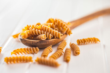 Naklejka premium Raw whole grain fusilli pasta. Uncooked pasta on wooden spoon.