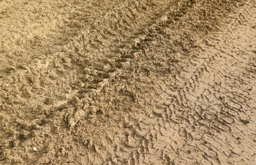Fototapeta na wymiar Wheel track on mud. Traces of a tractor or heavy off-road car on brown mud in a wet meadow