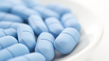 Heap of Blue pills in white plate close up. Pharmaceutical production