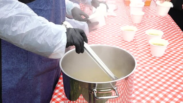 A pot of soup for needy people. Sharing soup to people. Homeless people get a bowl of soup
