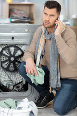 man sitting next to dishwasher on the phone