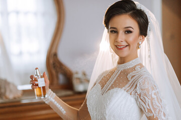 A bride in an elegant dress with long sleeves holding a bottle of luxurious perfume