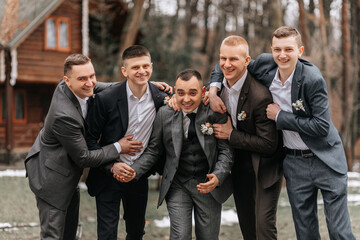 The groom and his friends are dressed in suits, fooling around in nature during a photo shoot. A...