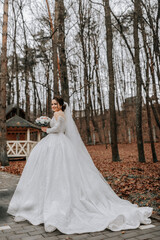 The bride is wearing a white voluminous dress with a long train, holding a bouquet and posing while walking in the forest. Winter wedding.