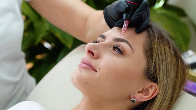 Beautician hand doing eyebrow permanent makeup on a pretty woman face