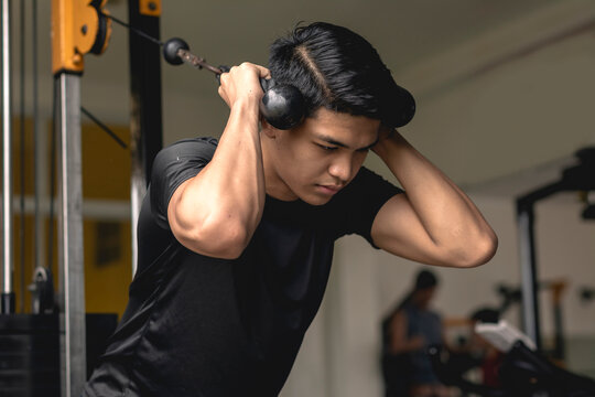 A young handsome asian man does standing rope crunches. Core exercises at the gym.